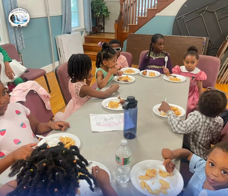 Une dizaine d'enfants attablés après le culte, assiettes de pâtes et de poulet, une feuille de coloriage posée au milieu de la table.